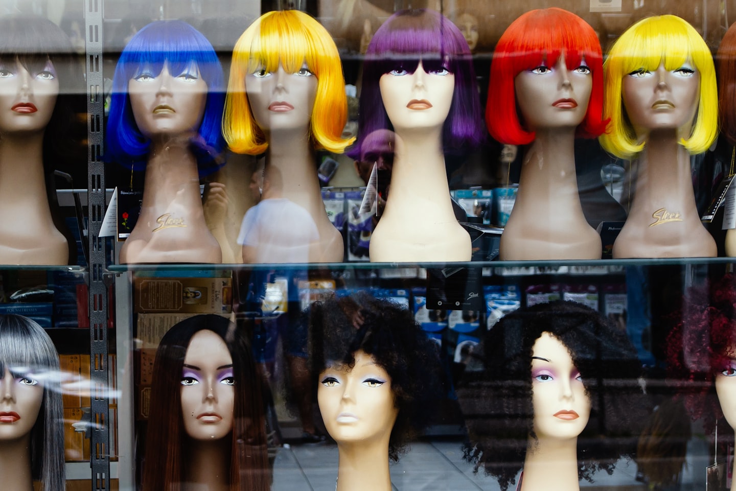 Mannequin heads display colorful wigs in a storefront window.