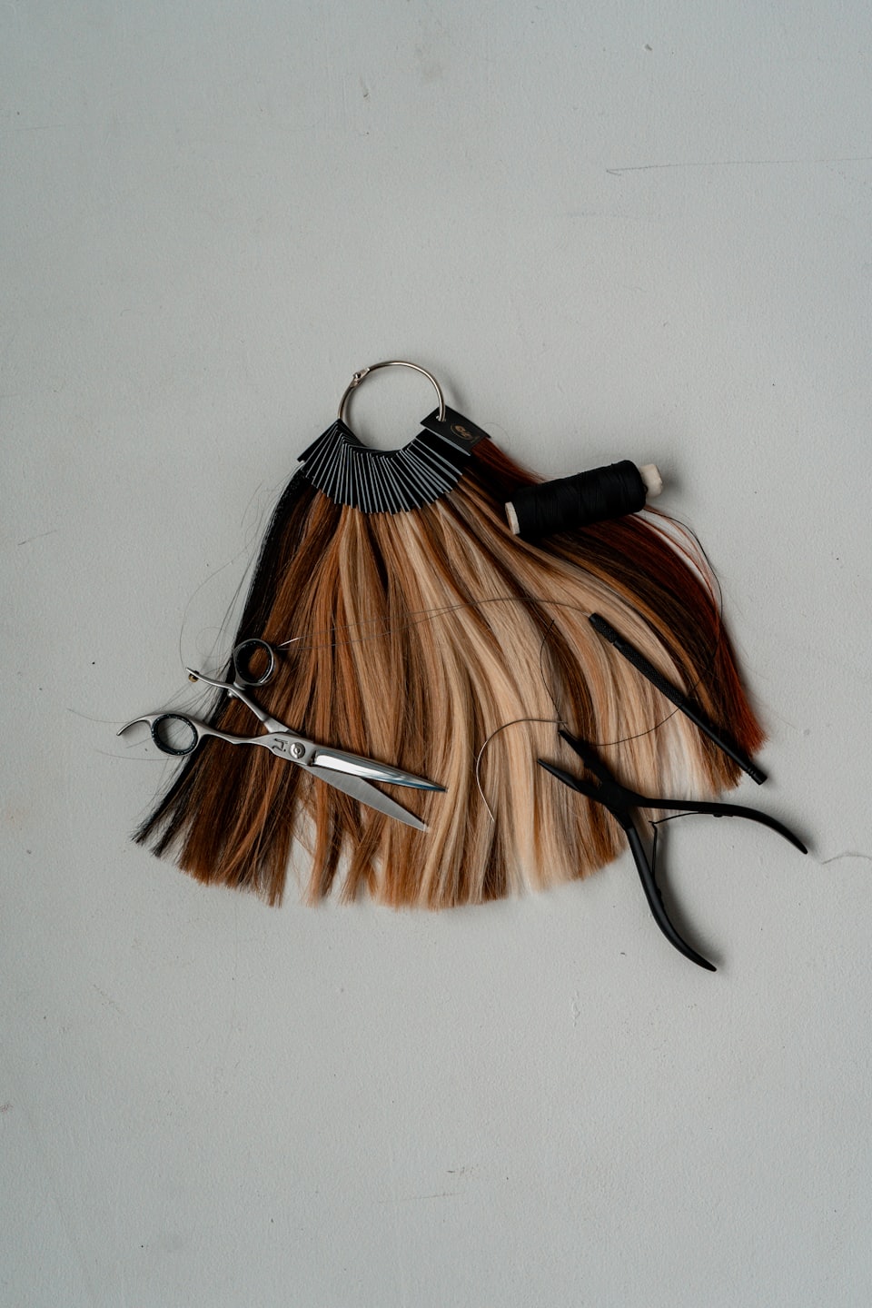 Hair extension color ring with professional tools on grey surface.