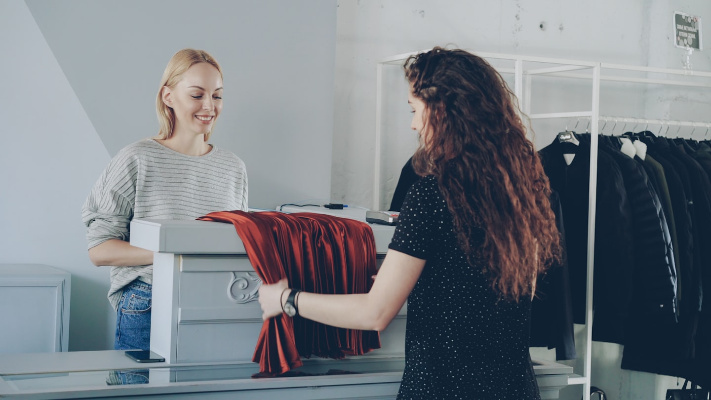 Customer shows red garment to smiling shop assistant at counter.