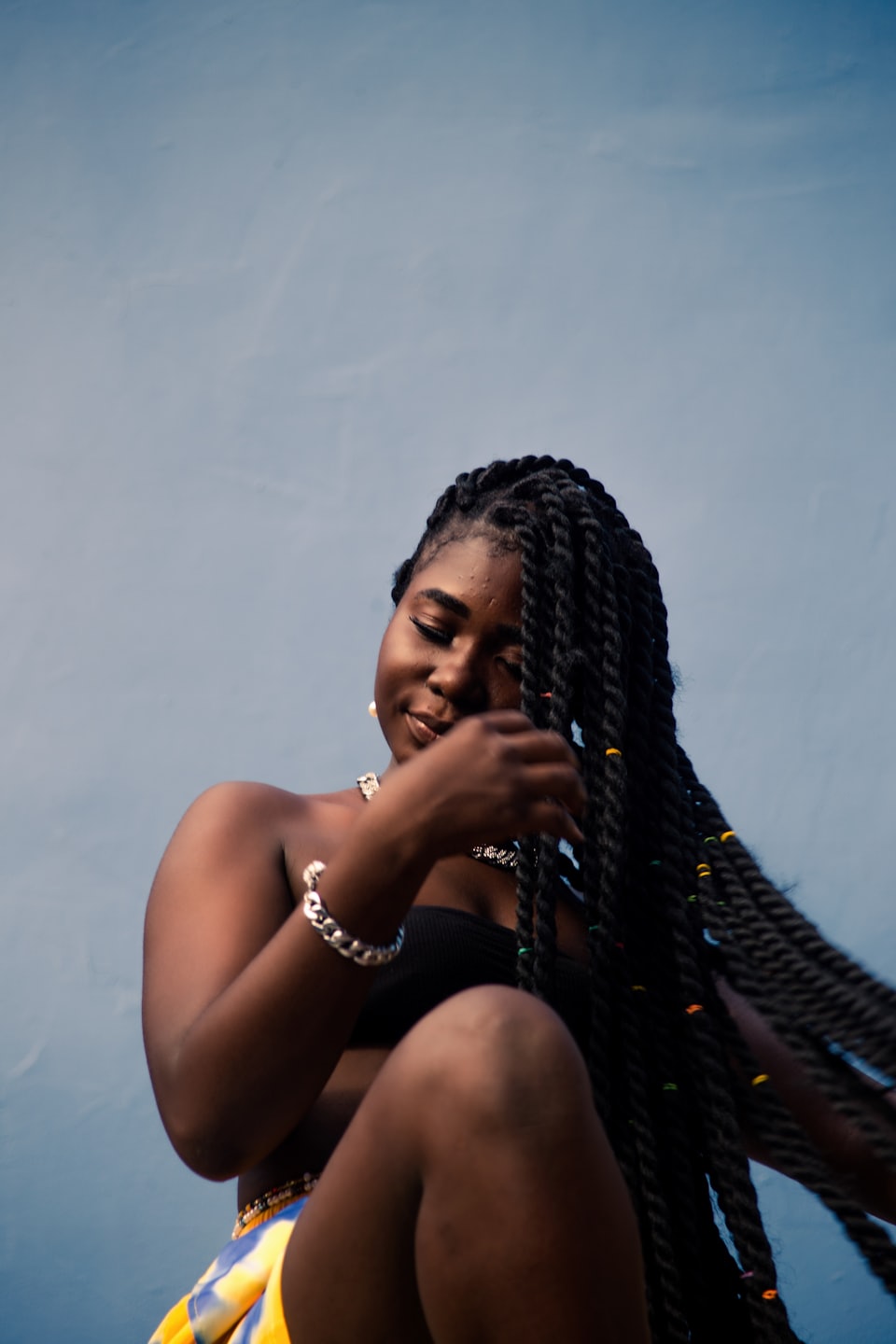 Woman with long braids smiles while touching her hair.