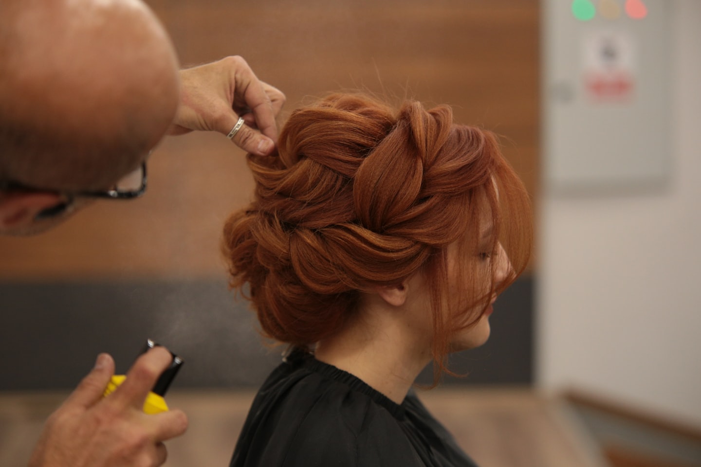 Stylist braids auburn hair into an updo at a salon.