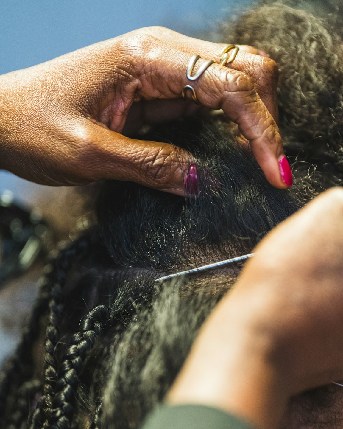 Stylist carefully braiding dark hair at the scalp.
